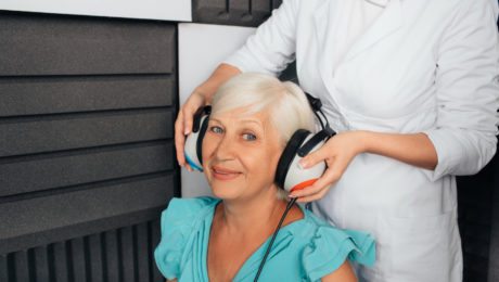 Kobieta podczas zakładania słuchawek przez protetyka słuchu w celu wykonania badania słuchu